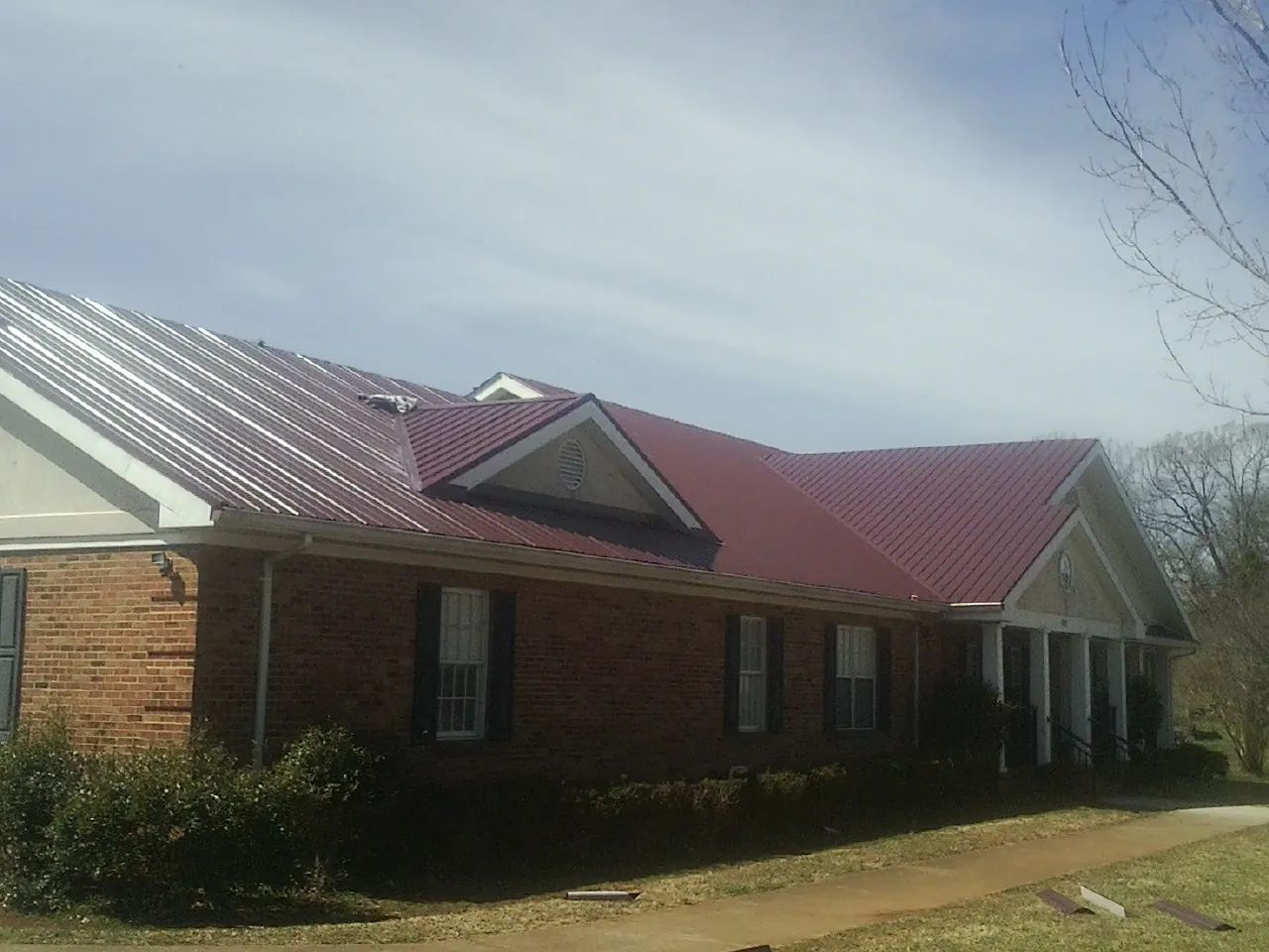 Red metal roof with gabled entries on a long brick building, from a Hail Damage Roof Repair job in Ashtabula