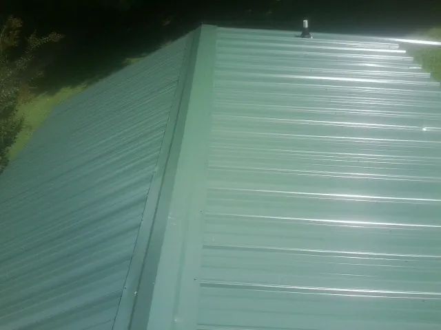 New green metal panels meeting at the ridge of a roof — Flat Roof Repair work by our crew in Ashtabula