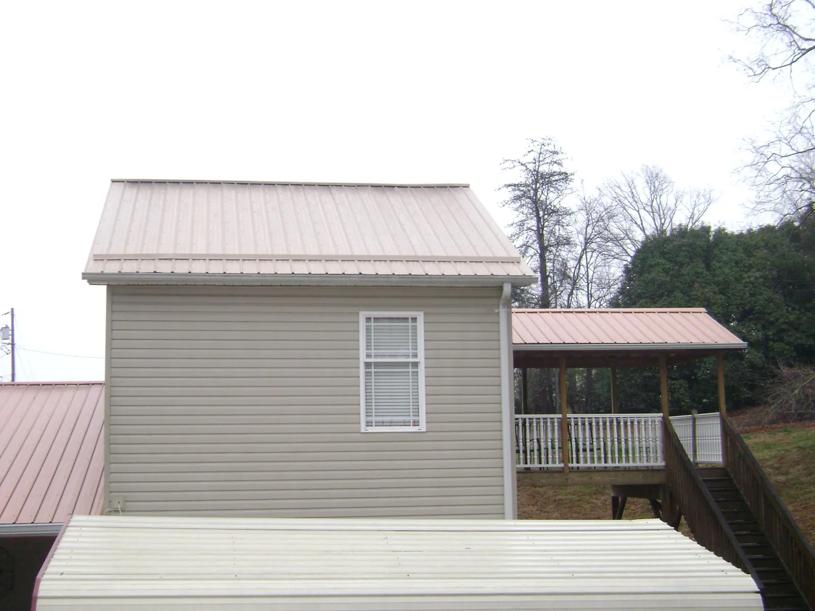 Tan metal roofs on a two story addition and attached porch, from a Roof Replacement job in Ashtabula